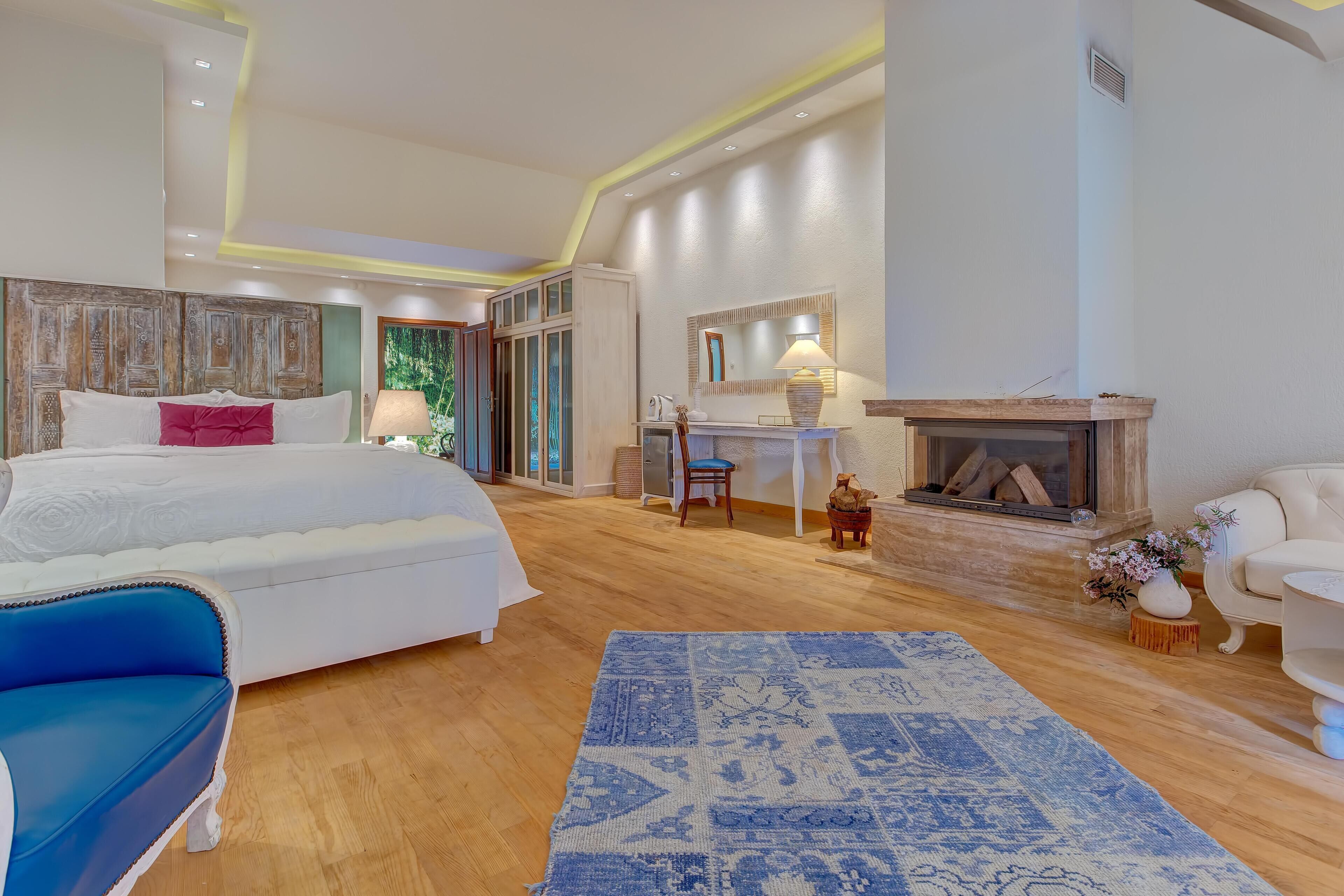 Um quarto espaçoso com uma cama grande, um sofá azul, uma lareira e uma escrivaninha com abajur.