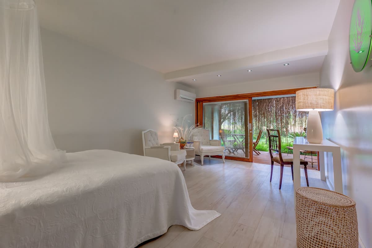 Quarto com cama, escrivaninha, cadeira e janela com vista para o verde.