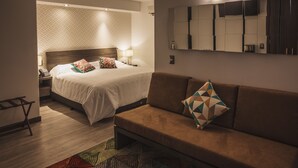 Une chambre d’hôtel avec un lit, un canapé, un tapis à motifs et un téléviseur fixé au mur.