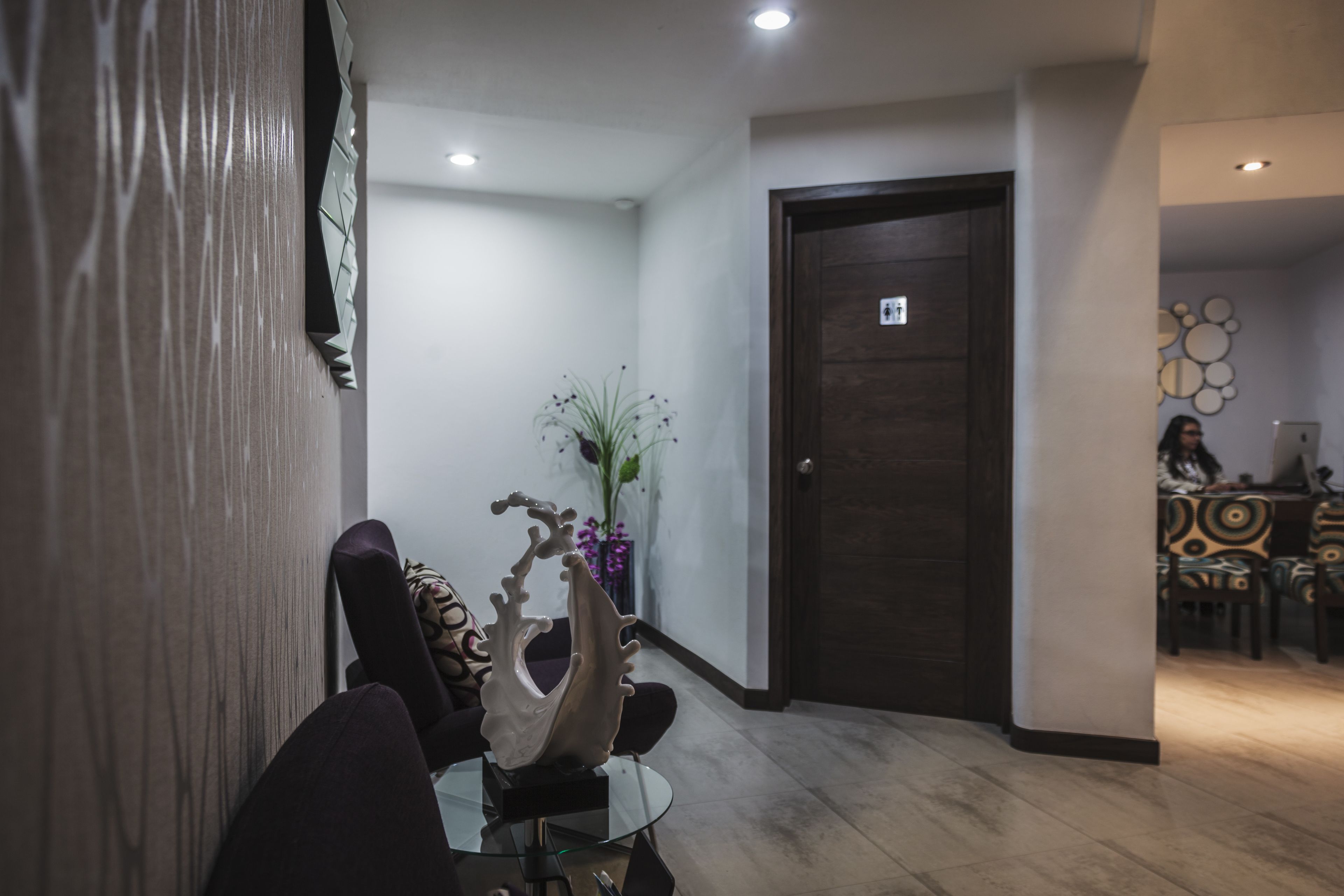 Een moderne hotellobby met een receptiebalie, een decoratieve muursculptuur en een eetgedeelte met gestreepte stoelen.