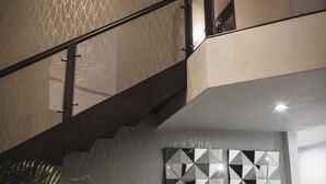 Un intérieur moderne avec un escalier, deux chaises noires, un vase décoratif et des œuvres d’art géométriques sur les murs.