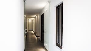Un couloir étroit et bien éclairé, doté d’un plancher en bois, de murs en verre et d’une porte au bout.