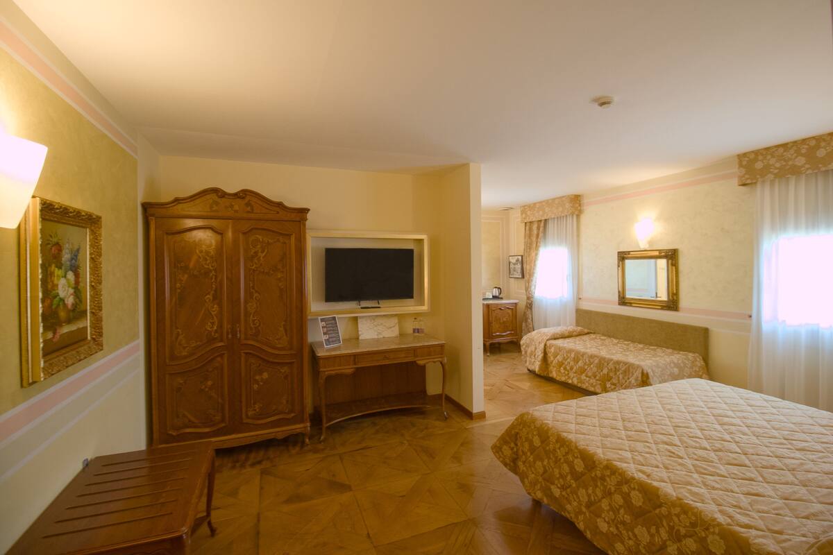 A hotel room with a wooden wardrobe, a desk with a television, two beds with floral bedding, and a framed picture on the wall.