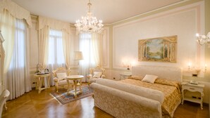 A spacious bedroom with a large bed, a chandelier, a painting on the wall, and a classic chair. - Hotel Villa Stucky (Mogliano Veneto)