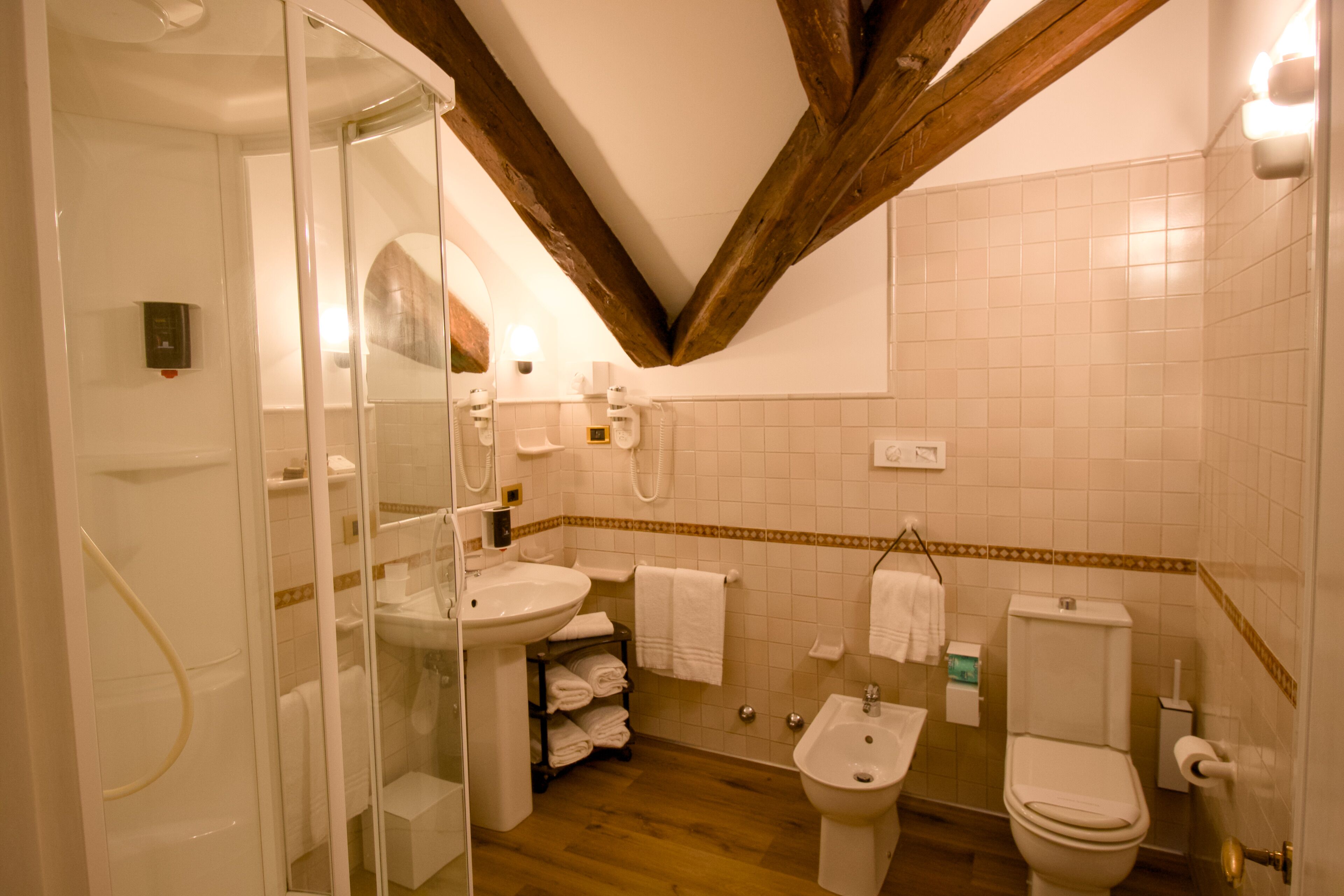 A bathroom with a shower, sink, bidet, toilet, and a towel rack.