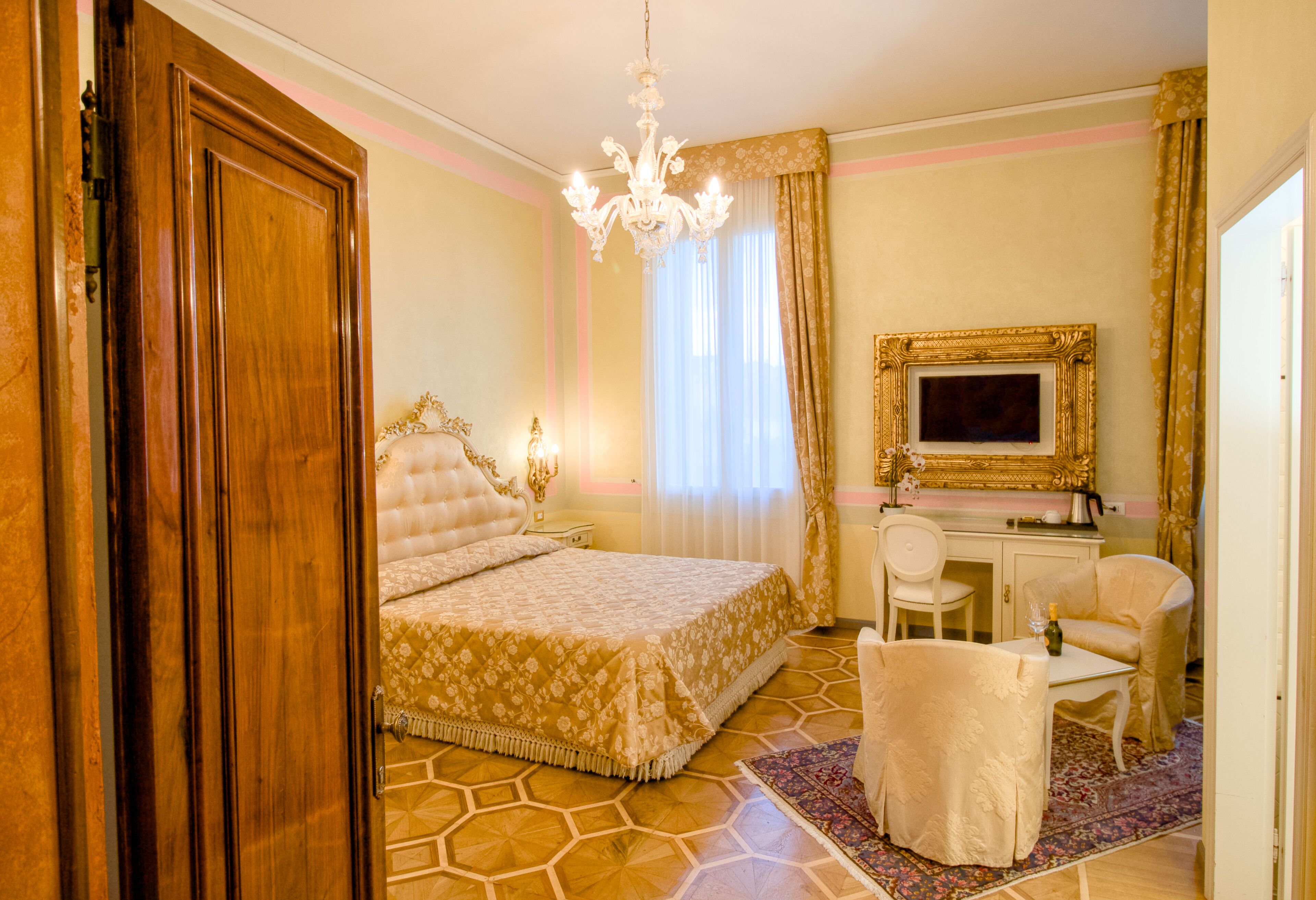 A hotel room with a bed, a desk, a chair, a chandelier, and a television.