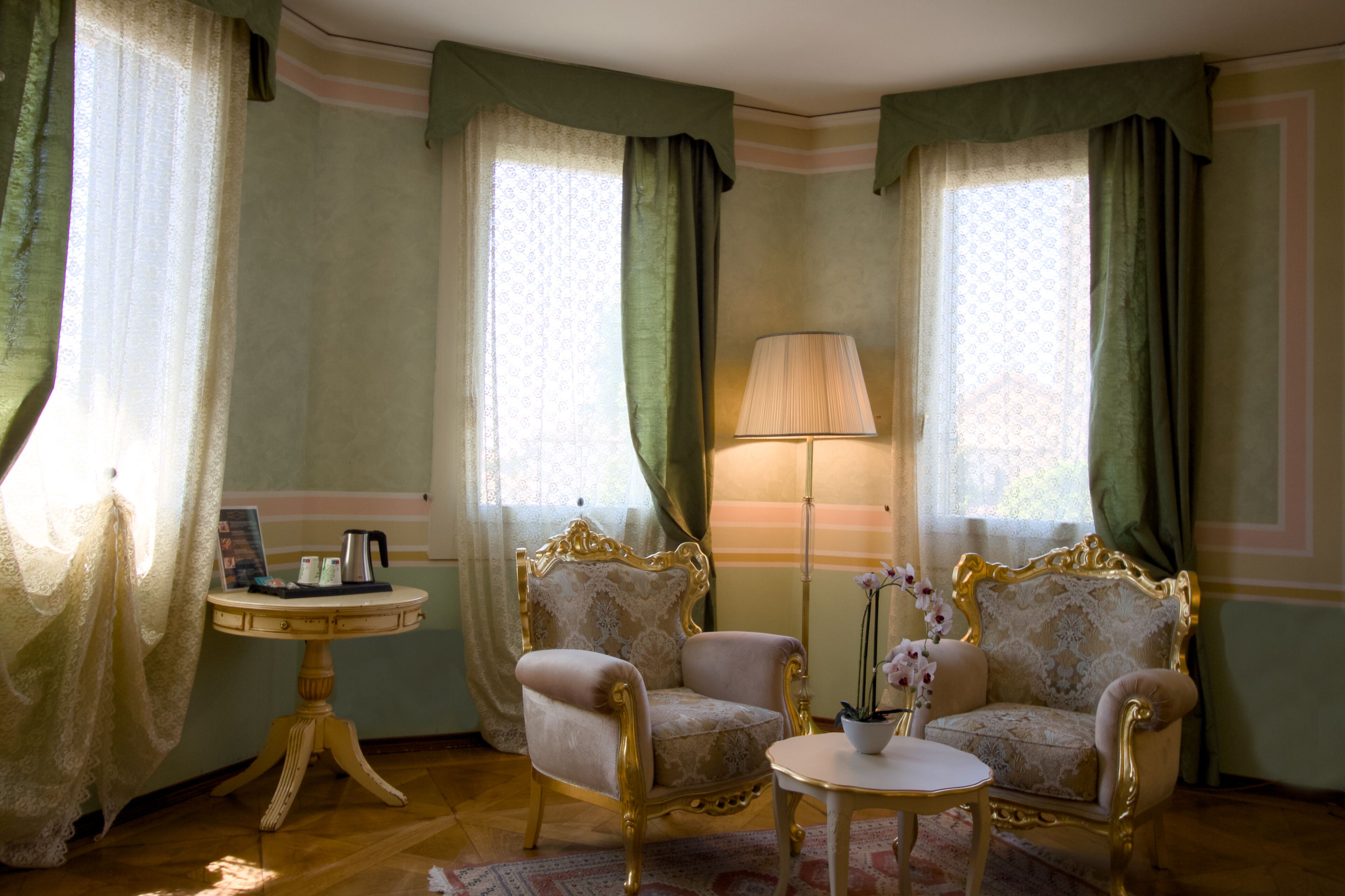 Een kamer met twee versierde fauteuils, een kleine ronde tafel en een vloerlamp.