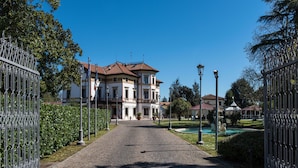 A cobblestone pathway leading to a large, multi-story building with a red-tiled roof, surrounded by greenery and a fountain. - Hotel Villa Stucky (Mogliano Veneto)
