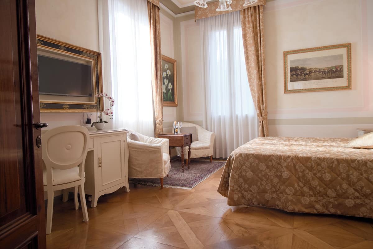 A hotel room with a bed, a desk, a chair, a television, and a painting on the wall.
