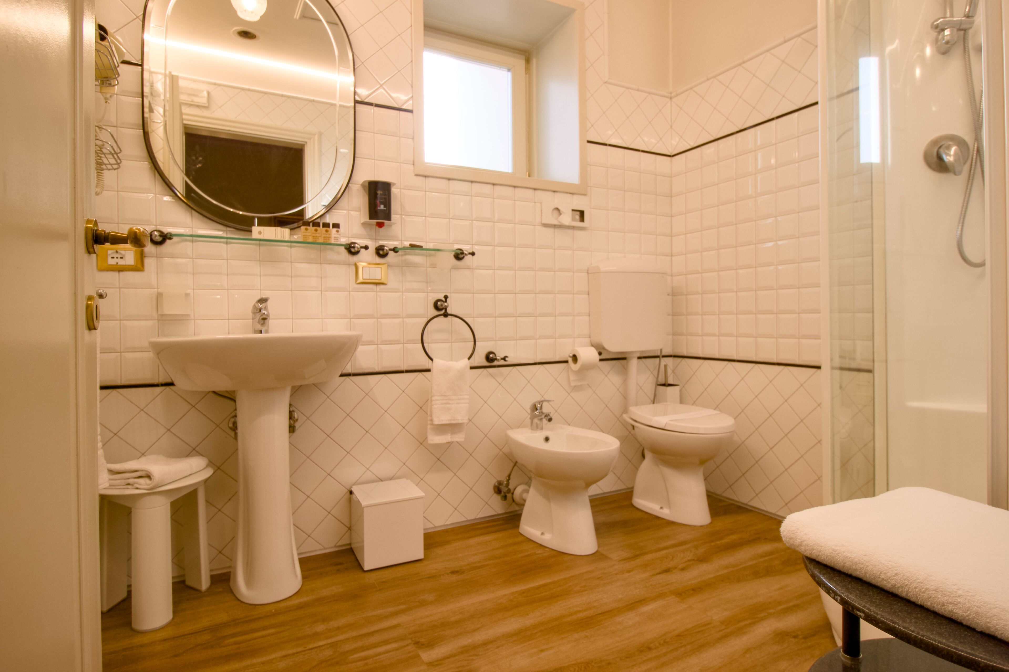 Bany modern amb un vàter amb peu de pedestal, dues vàteres, un bidet i una dutxa amb envàs de vidre.