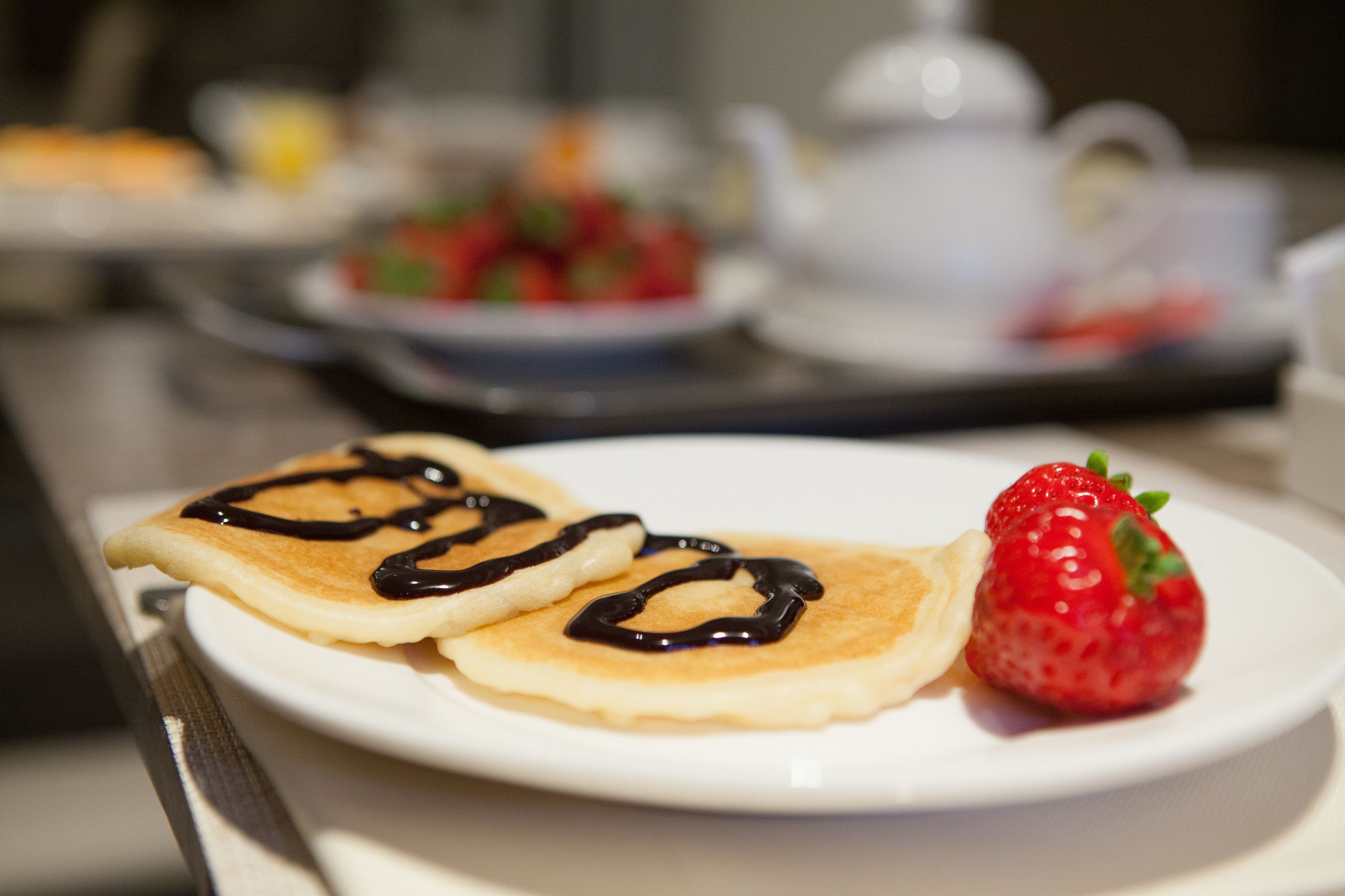A plate with two pancakes and a strawberry.