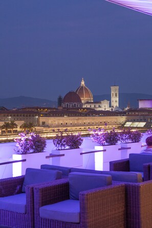 A rooftop terrace with wicker furniture and a view of a historic building with a dome and tower. - MH Florence Hotel & Spa (Florence)
