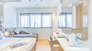 A modern hotel room with a bed, a desk, a chair, a small table with fruits, and a large mirror. - MH Florence Hotel & Spa (Florence)
