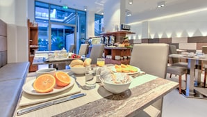 A breakfast setting with a table set for two, including plates of fruit, a bowl of cereal, and glasses of water. - MH Florence Hotel & Spa (Florence)