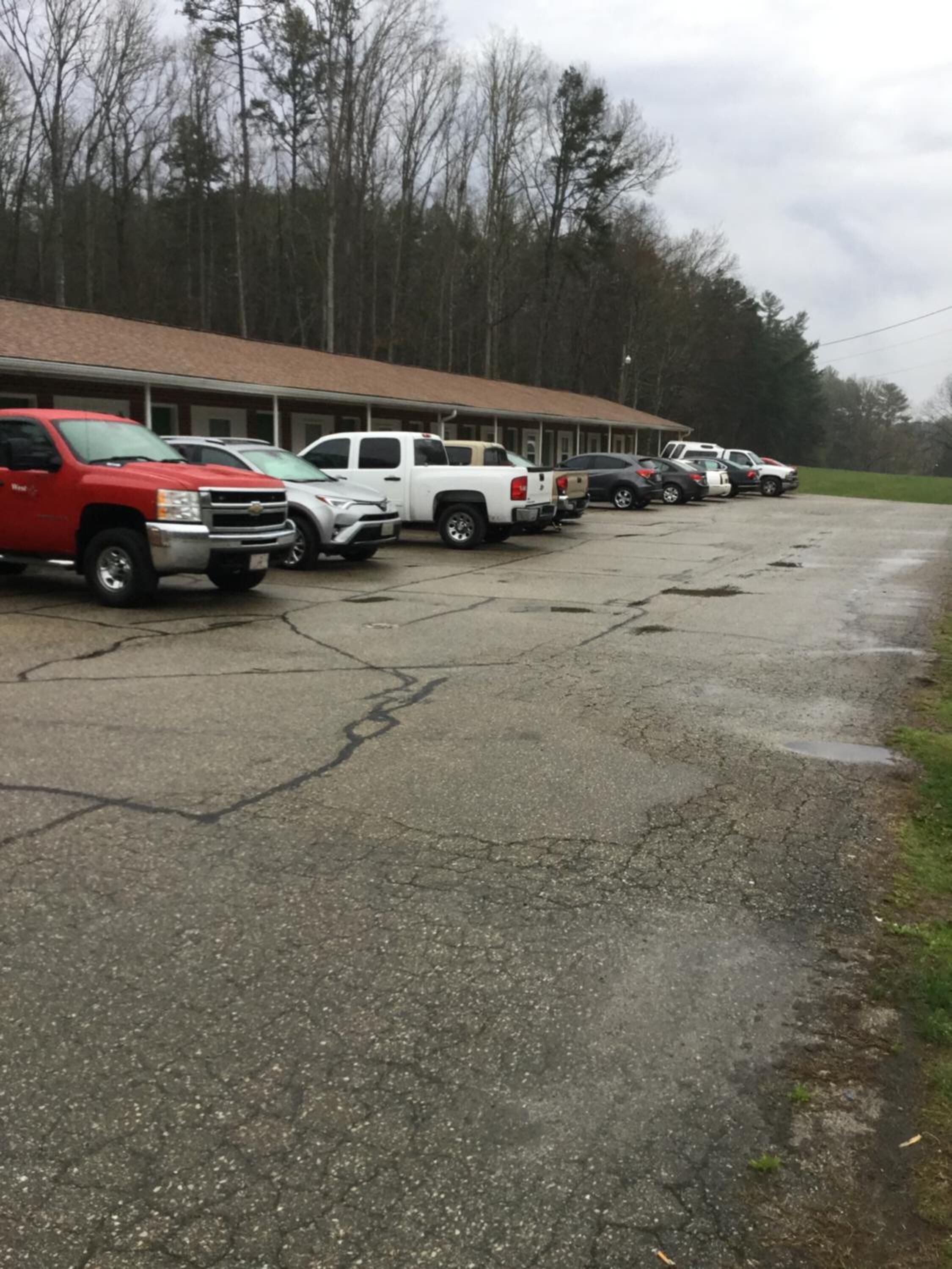 A parking lot with several vehicles, including trucks and cars, parked in front of a building with a brown roof.