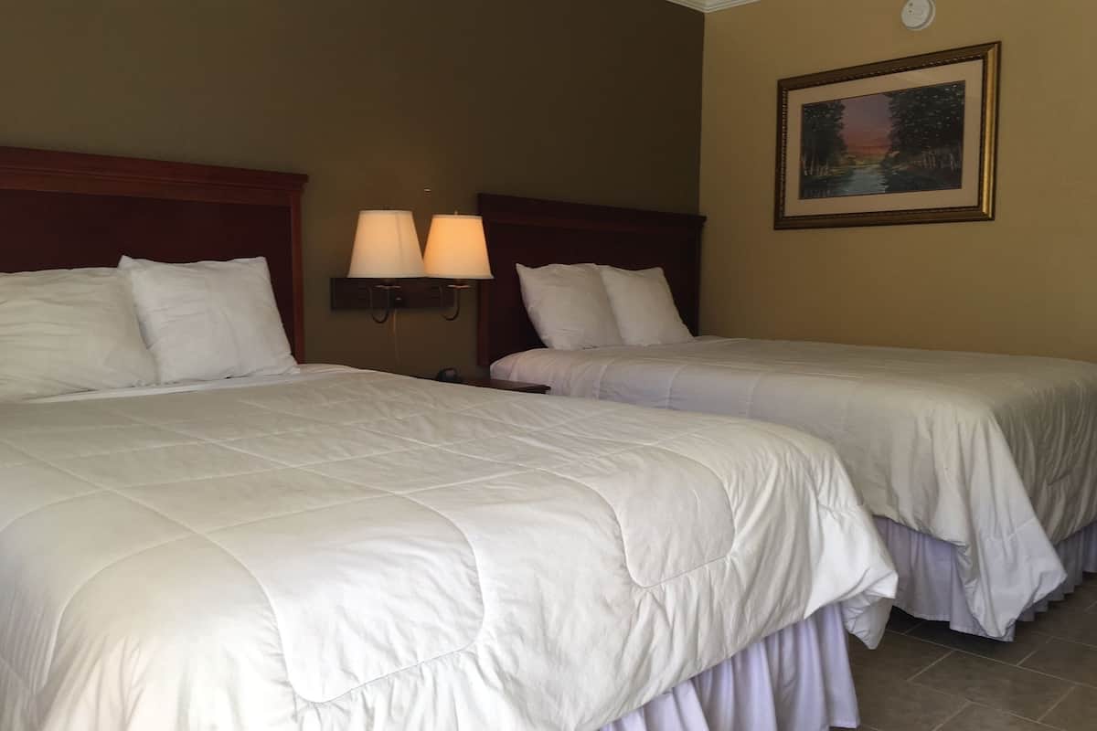 A hotel room with two beds, a headboard, wall-mounted lamps, and a framed picture on the wall.
