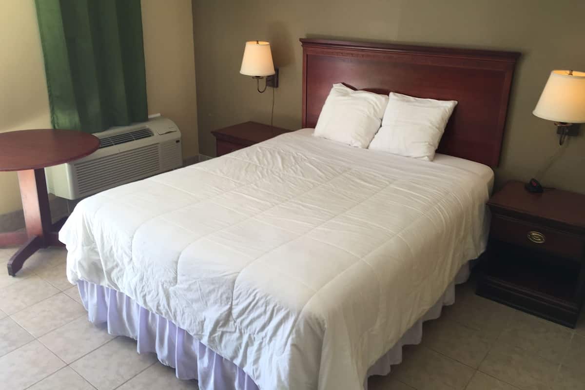 A hotel room with a large bed, two bedside tables, a round table, and an air conditioning unit.