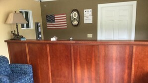 A reception area with a wooden desk, an American flag, a clock, and a blue patterned chair.