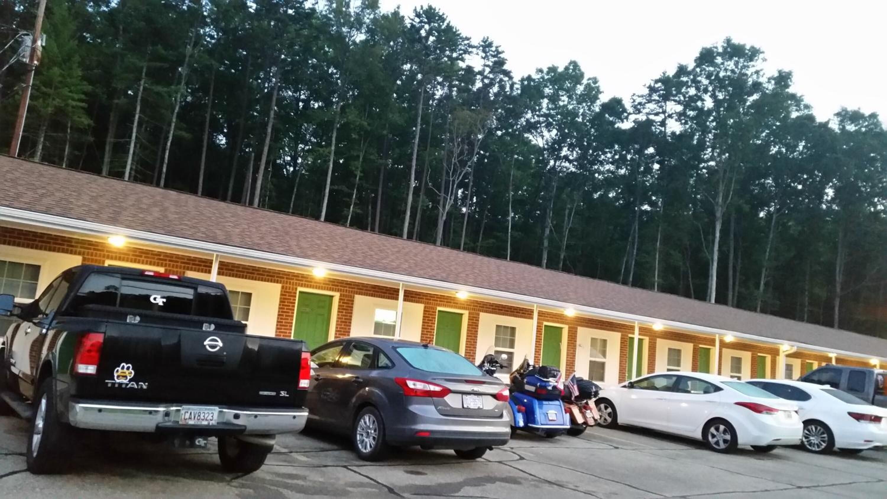 Un motel con fachada de ladrillo, varias habitaciones y un estacionamiento con diferentes vehículos.