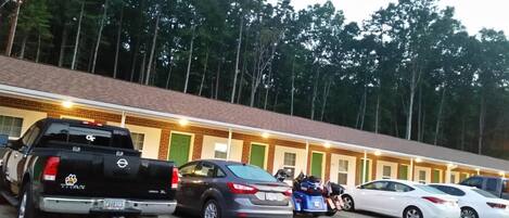 Un motel con facciata in mattoni, diverse camere e un parcheggio con vari veicoli.