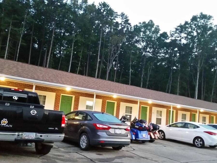 Un motel con fachada de ladrillo, varias habitaciones y un estacionamiento con diferentes vehículos.