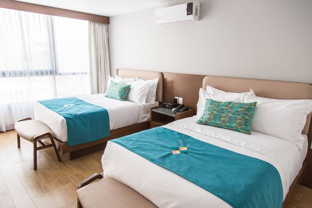 Habitación de hotel con dos camas, una mesita de noche con teléfono, una silla y una ventana con cortinas.