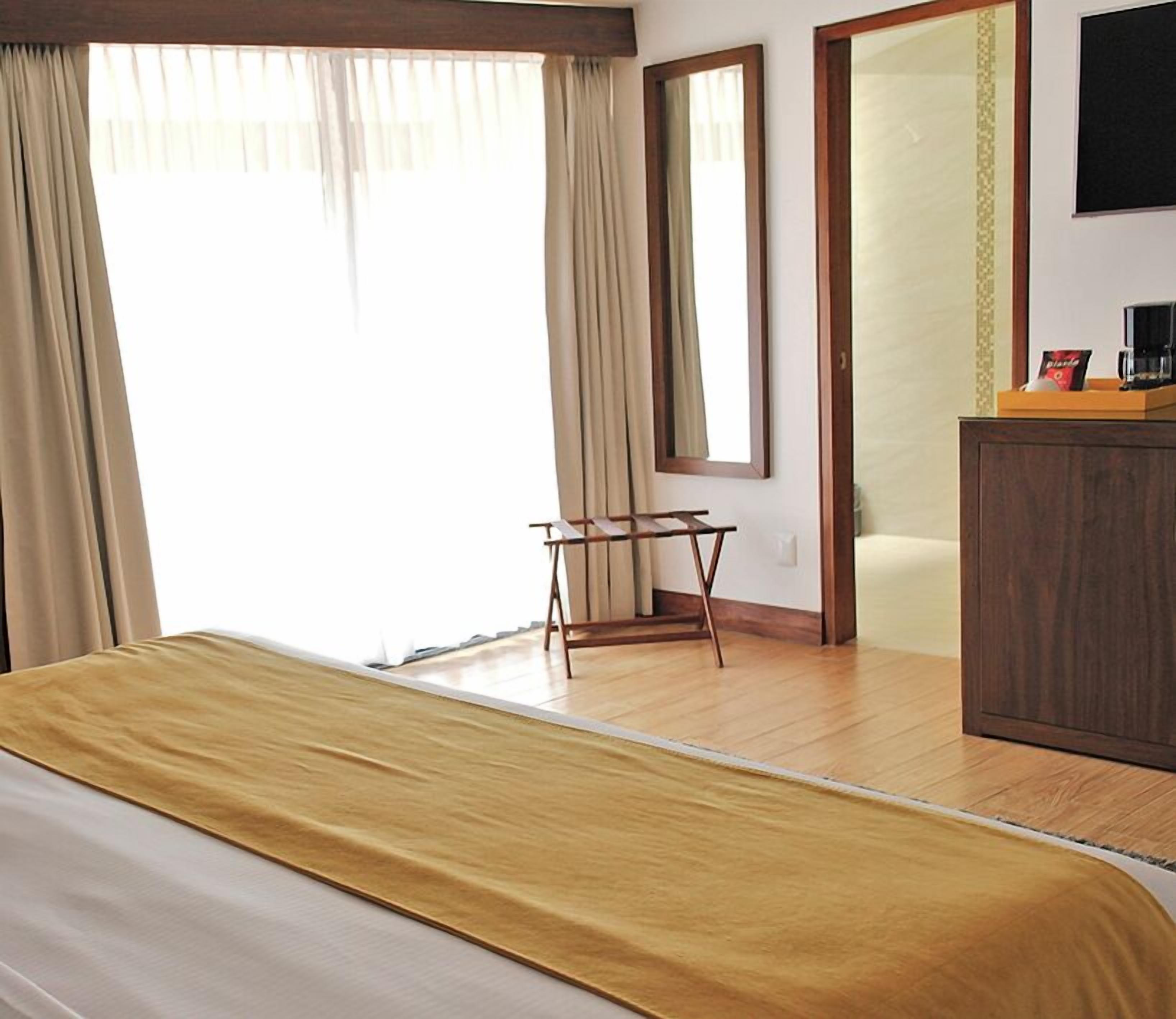 Ein Hotelzimmer mit Bett, kleinem Tisch, Spiegel, Kleiderschrank und Blick ins Freie.