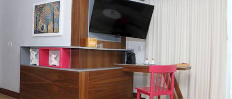 A modern room with a wooden desk, a flat-screen TV, a pink chair, and a painting on the wall.