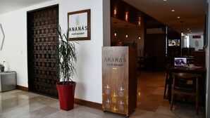 Un área de recepción con un mostrador de madera, una planta en maceta y un letrero en la pared para el restaurante 'Ananas'.