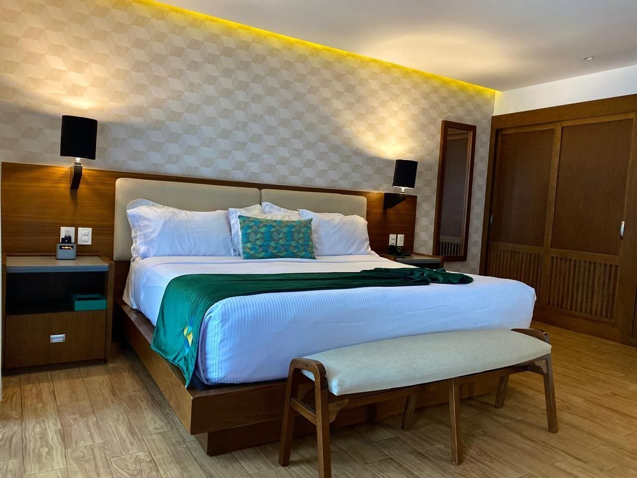 Une chambre d’hôtel comprenant un lit, des tables de chevet, un banc et une armoire.