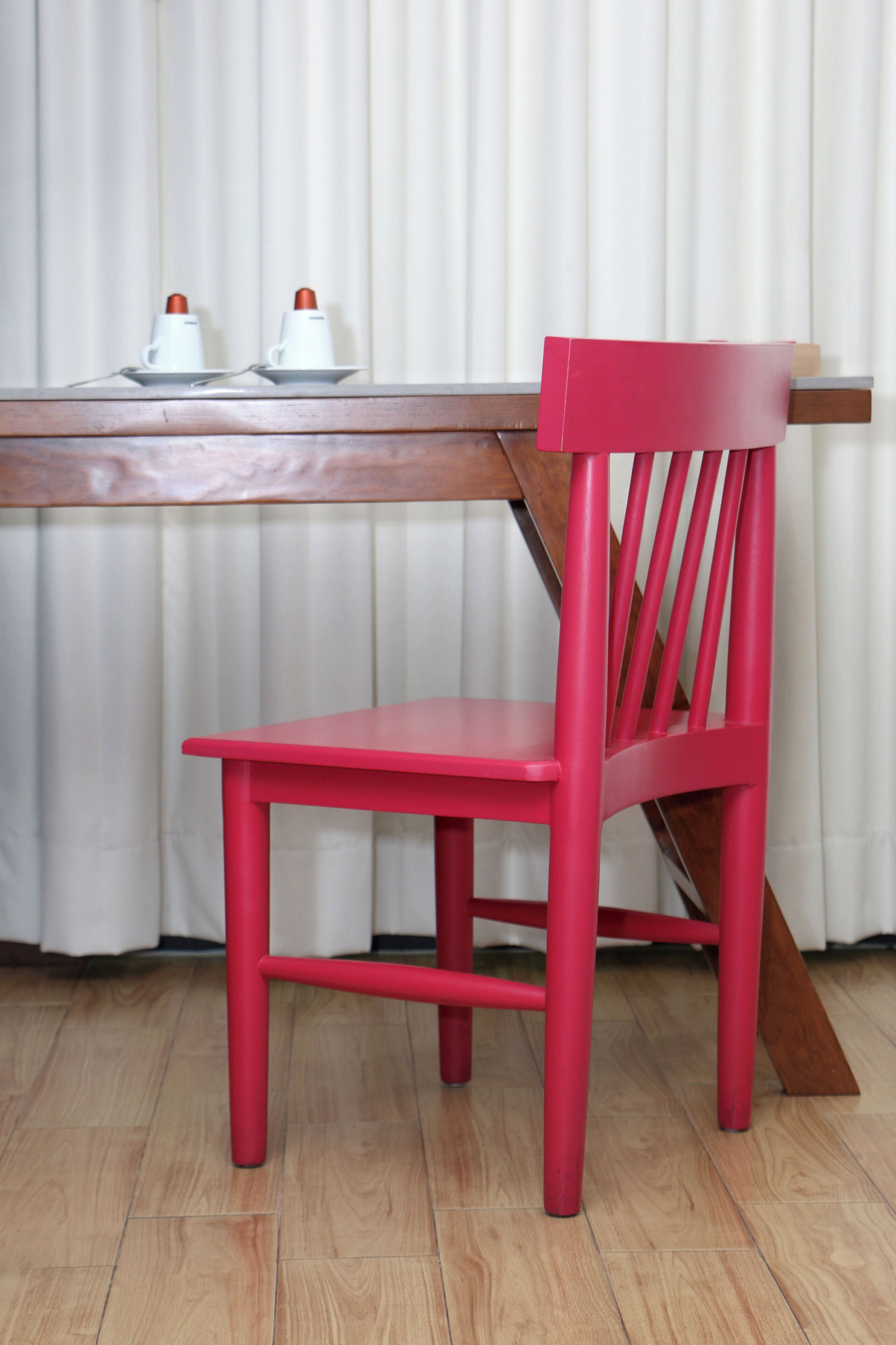 A red chair and a wooden table with two white cups and saucers.