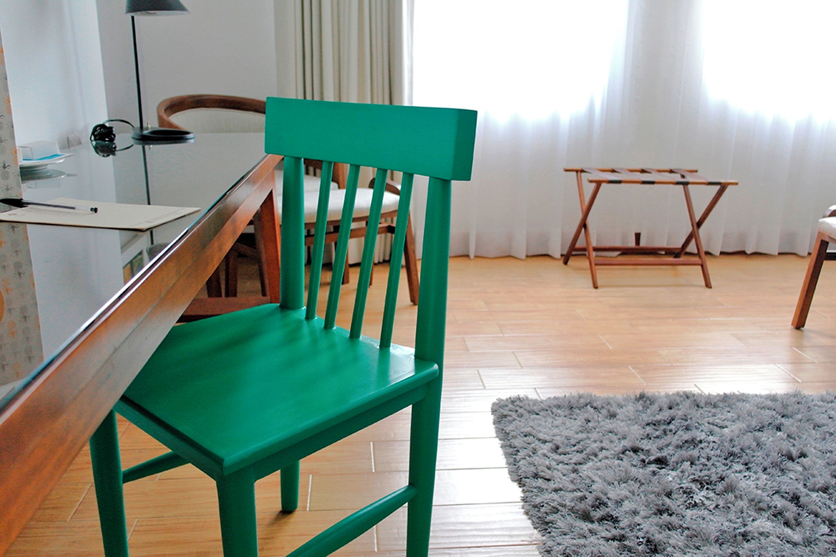 A room with a wooden desk, a green chair, a grey rug, and a wooden table with a white cloth.