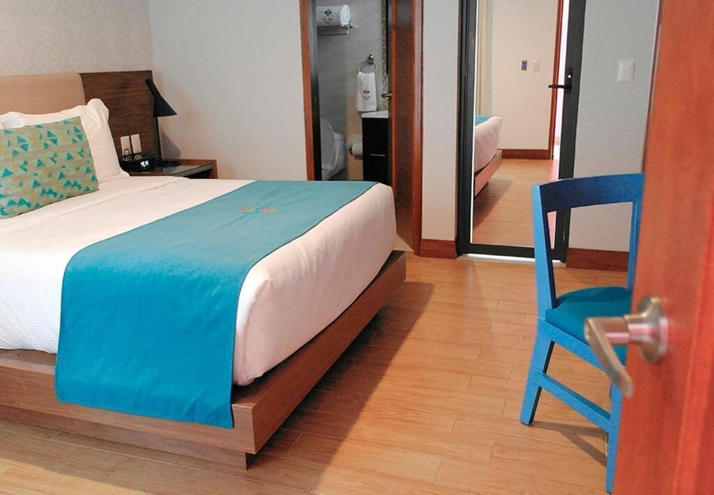 A hotel room with a bed, a chair, a nightstand, and a bathroom visible through an open door.