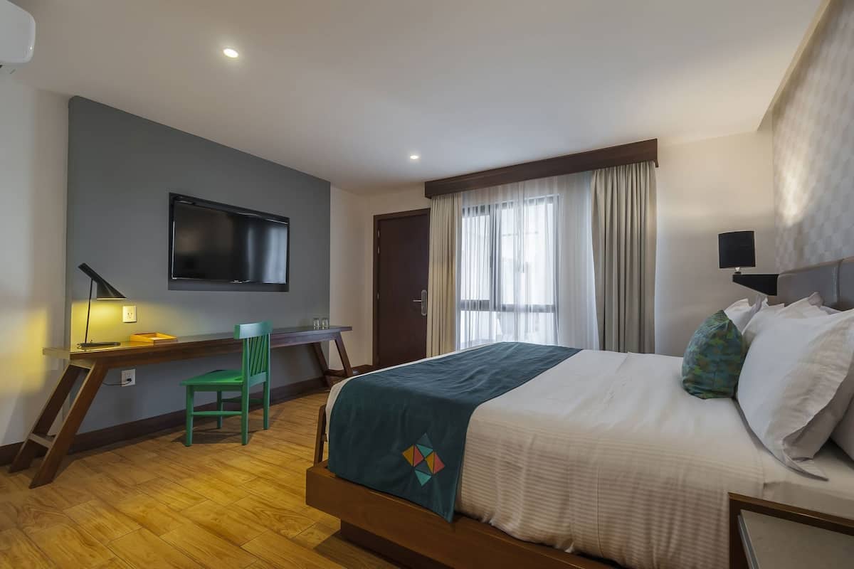 Una habitación de hotel con cama, escritorio, silla, televisión y cortinas.