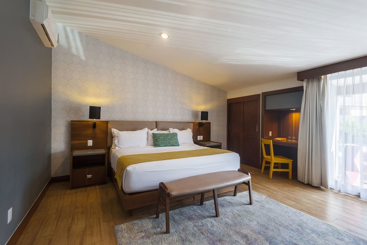 Habitación de hotel con una cama grande, un escritorio, una silla, un televisor y una ventana con cortinas.