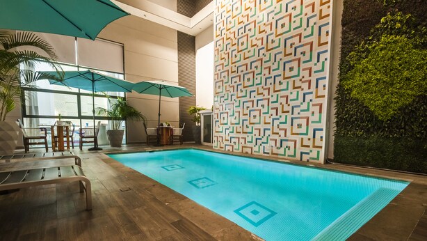 Una piscina interior con un muro de diseño geométrico, suelo de madera y sillones de descanso.