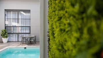 Zona de piscina con una mesa y sillas, una planta en maceta y vistas a un edificio con grandes ventanales.