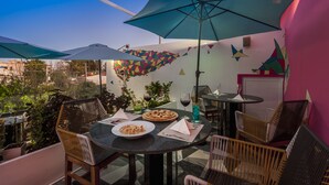 Un patio al aire libre con mesas redondas, sillas de mimbre y sombrillas.