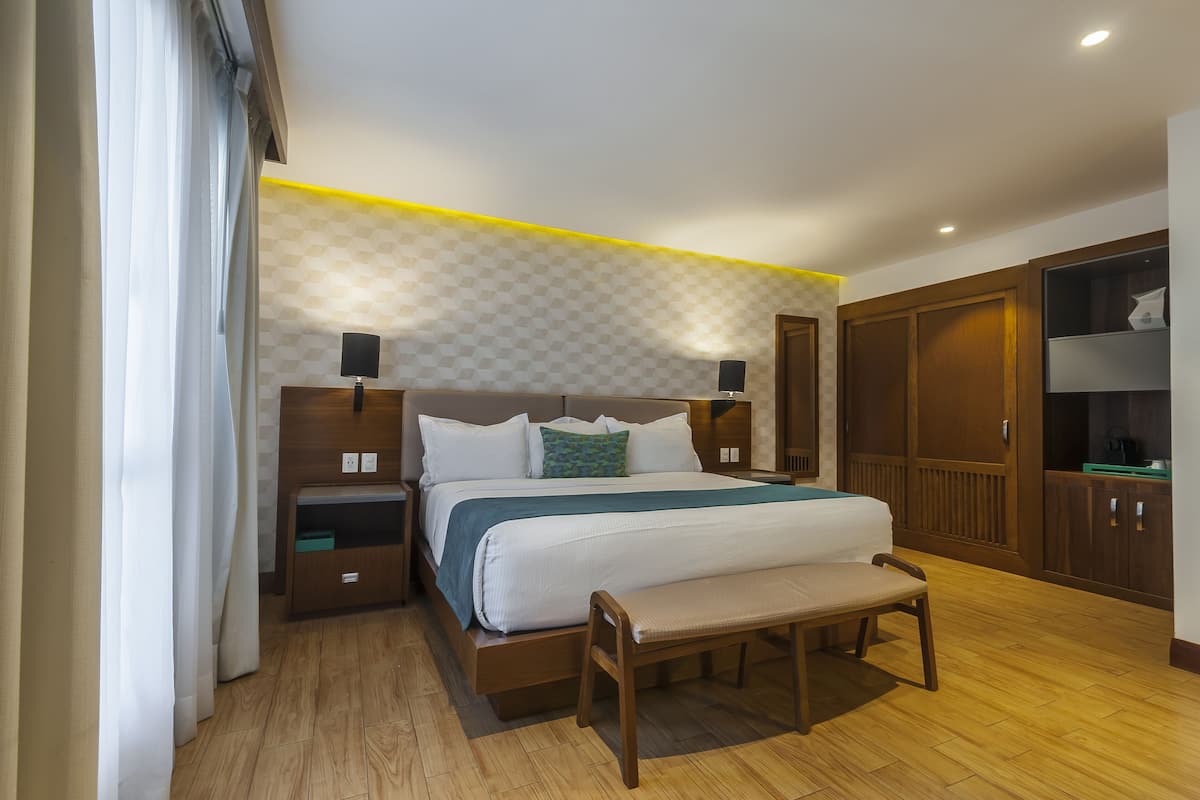 Un dormitorio ordenado con una cama grande, mesitas de noche, un banco y armarios de madera.