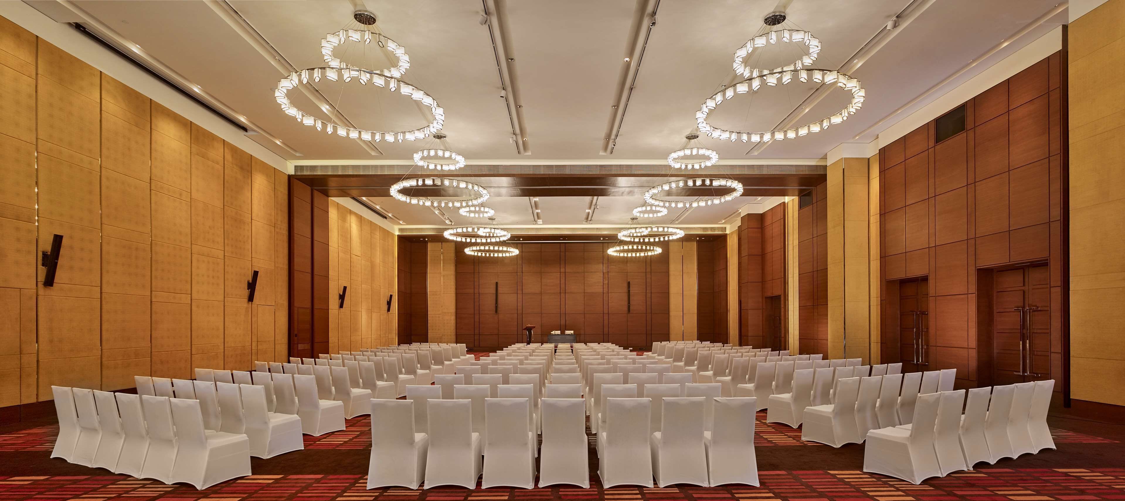 A conference room with rows of white chairs, a carpeted floor, and circular chandeliers.