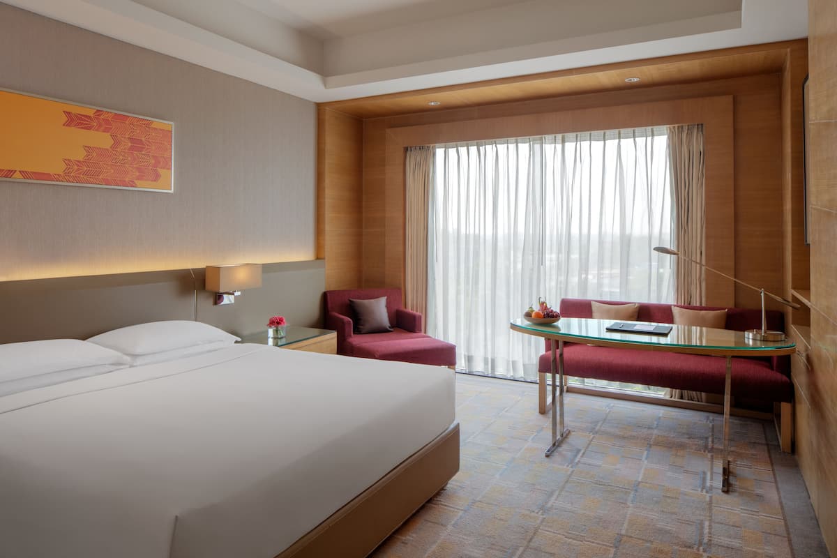 A hotel room with a large bed, a desk with a chair, a sofa, and a large window with curtains.