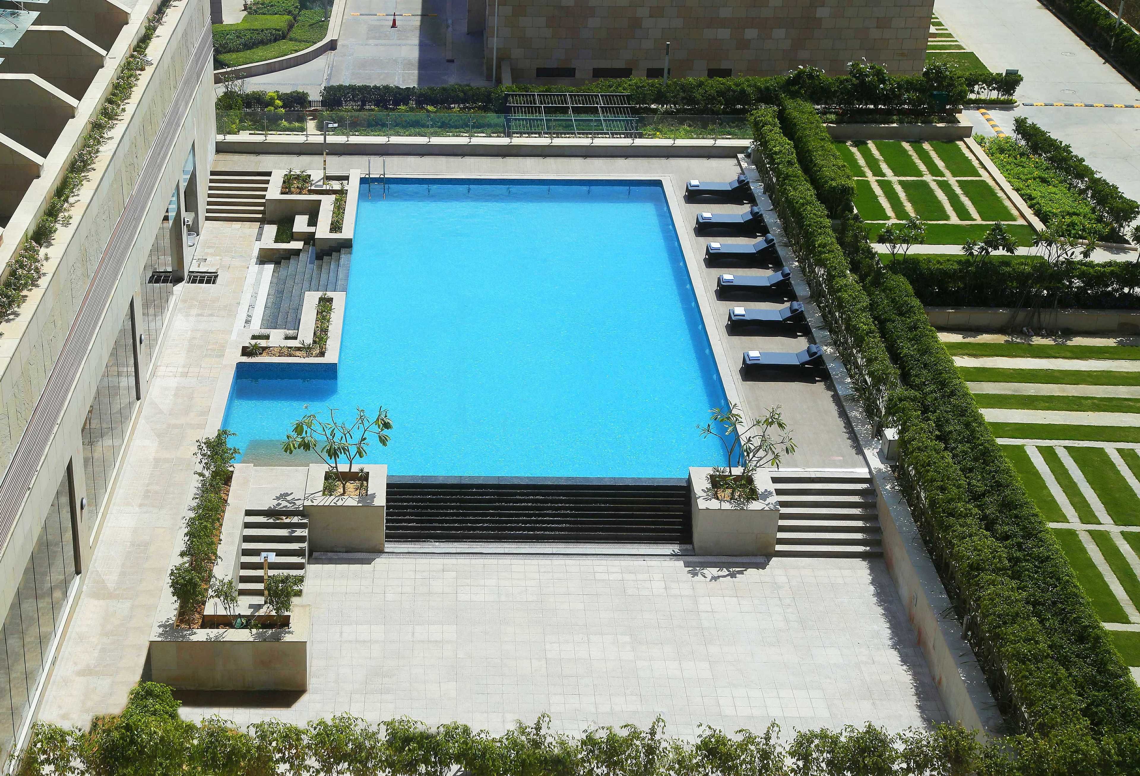 A large rectangular pool with steps leading into it, surrounded by a landscaped garden and a building with a modern design.