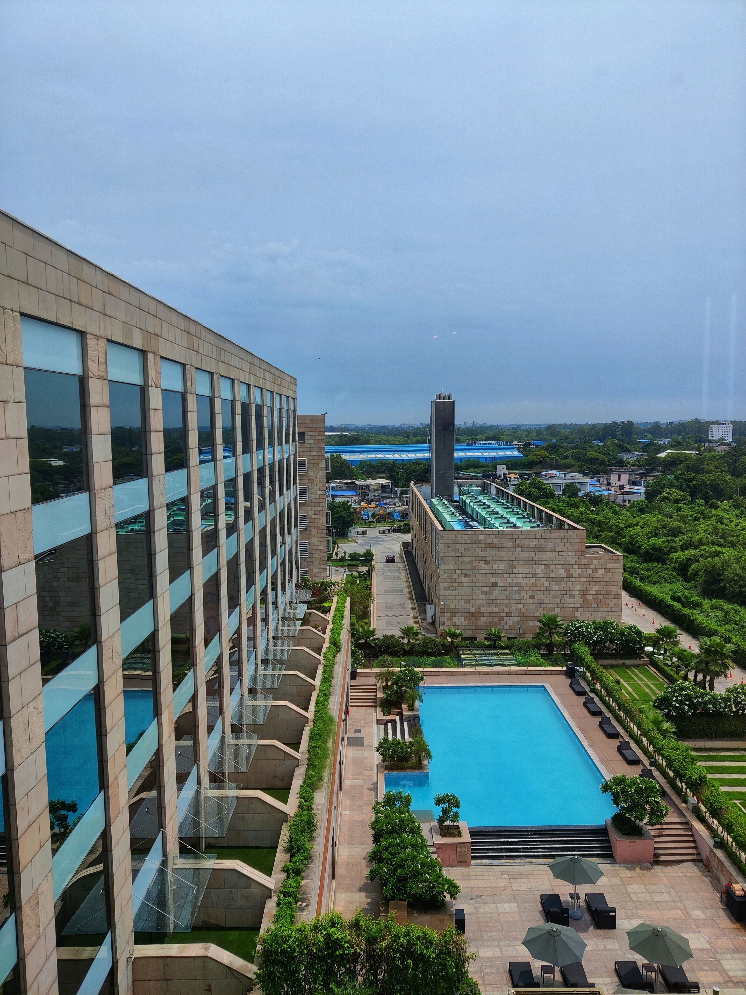 Ein modernes Hotel mit Dachpool, einem großen Glasgebäude und Blick auf eine Brücke und Grünflächen.