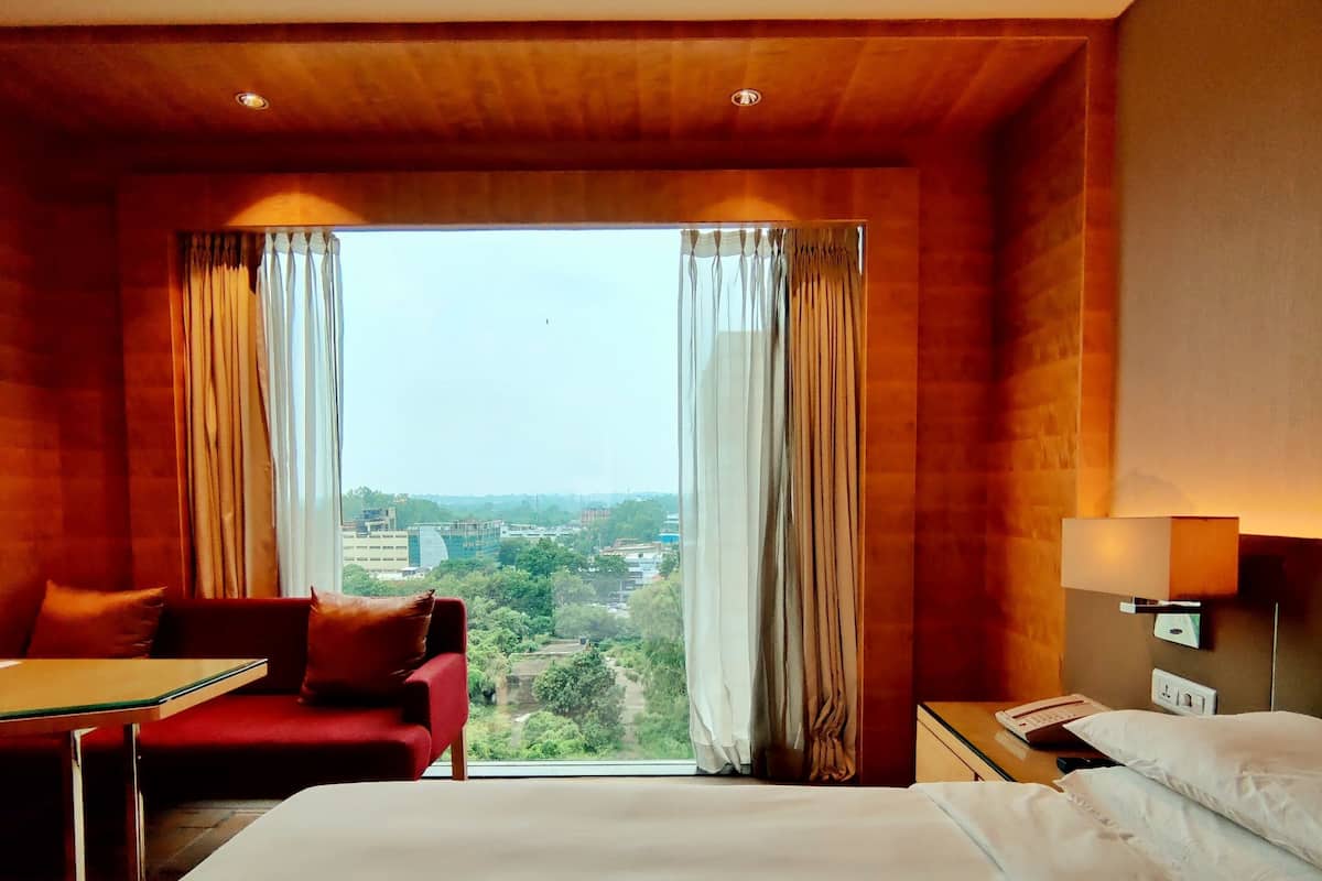 A hotel room with a large bed, a red sofa, a small table, and a nightstand with a lamp.