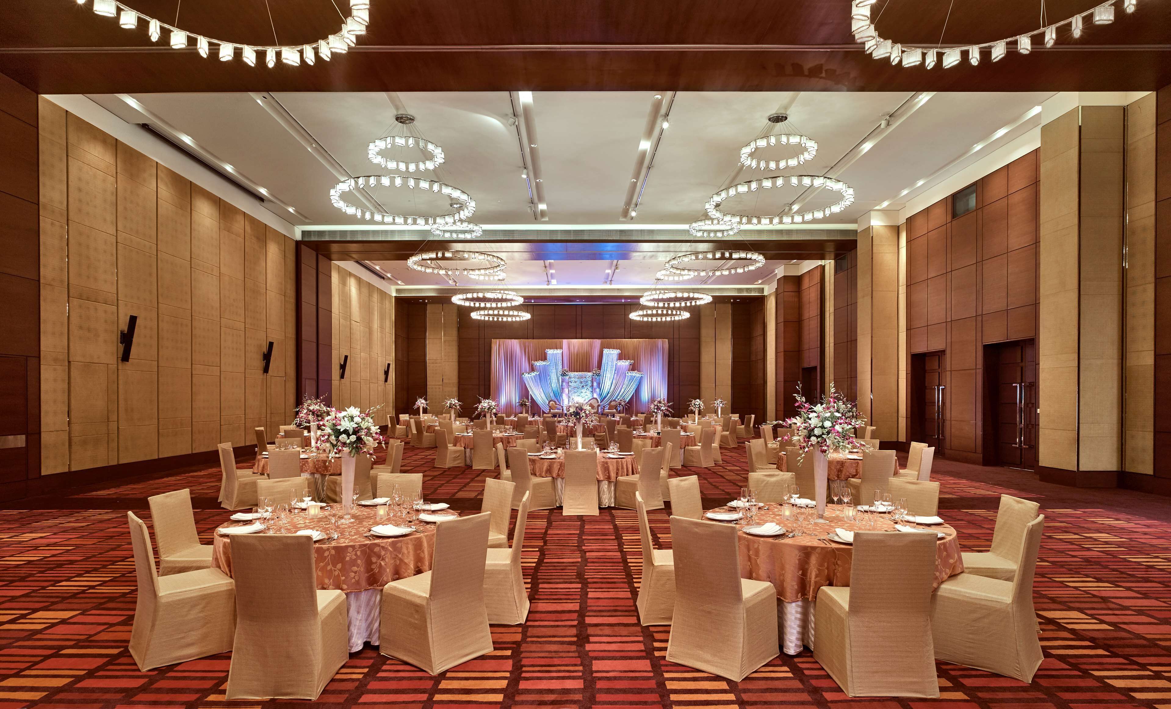 A spacious banquet hall with round tables, chairs, and a stage with draped curtains.