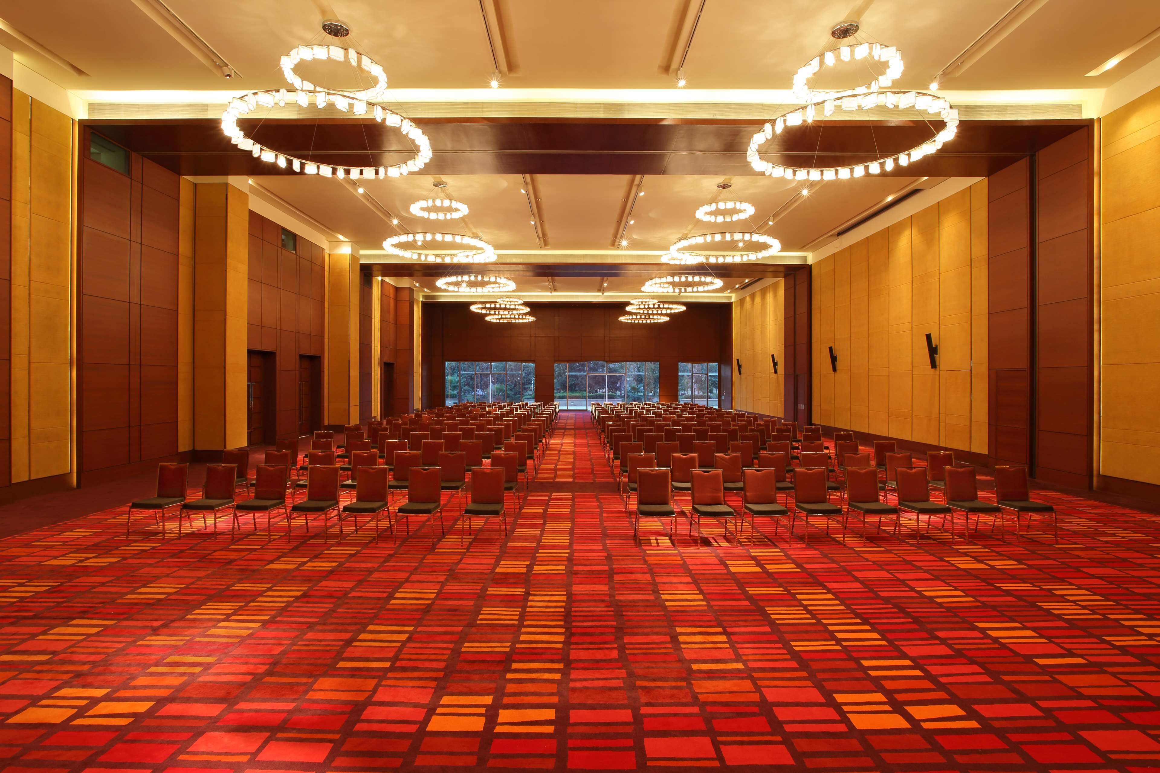 A conference room with rows of chairs, a patterned carpet, and multiple chandeliers.