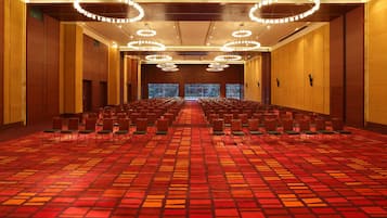 A conference room with rows of chairs, a patterned carpet, and multiple chandeliers.