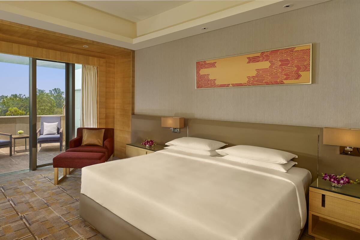 A hotel room with a large bed, two bedside tables, a chair, a balcony with a view, and a decorative wall piece.