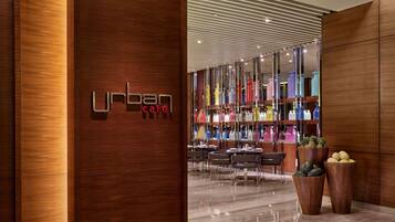 Un interior moderno con un mostrador de recepción de madera, una zona de cafetería con botellas de colores y un suelo de mármol pulido.