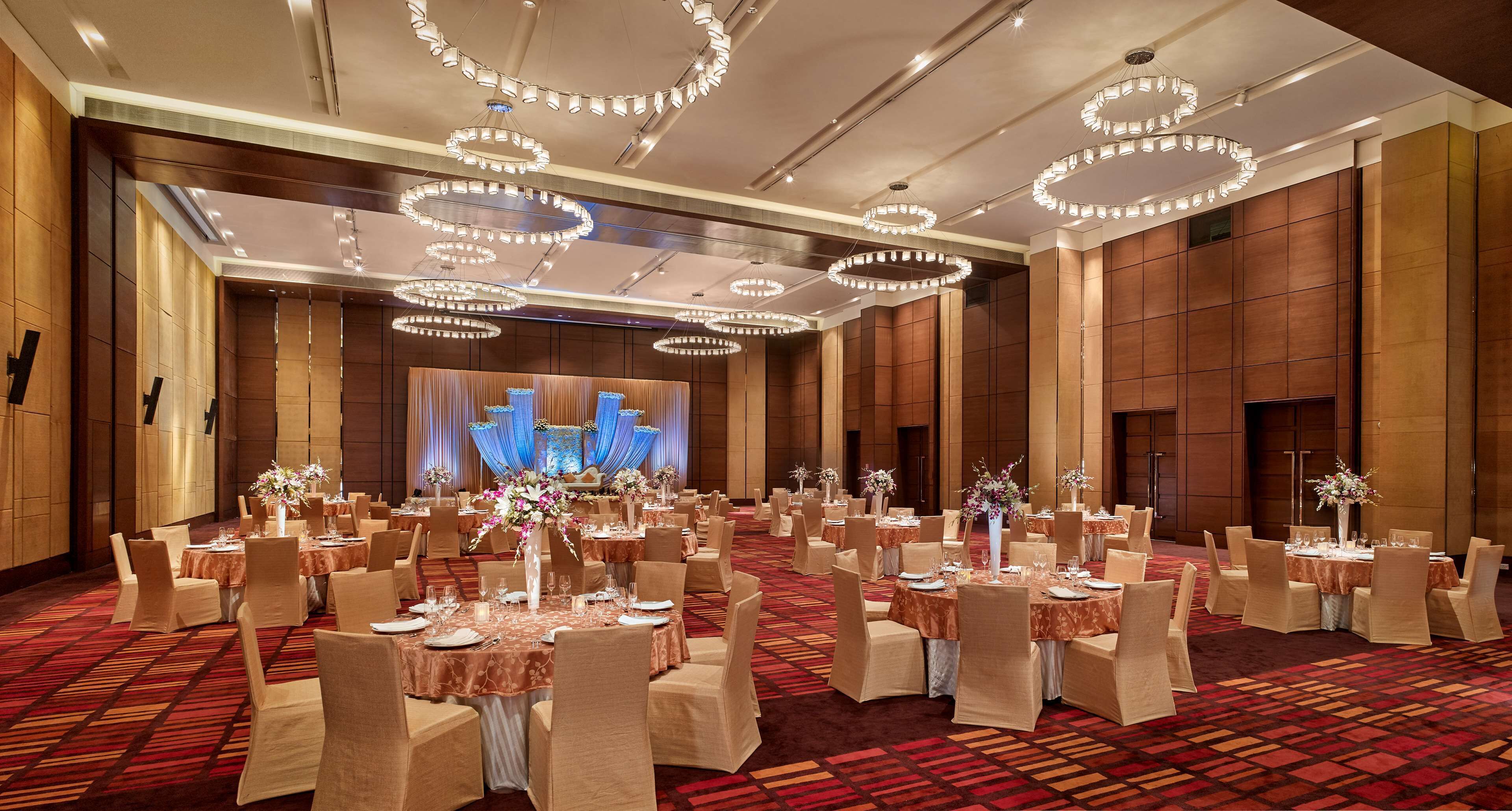 A banquet hall with round tables, chairs, and chandeliers.